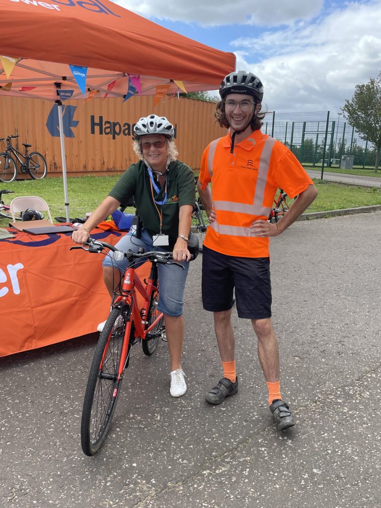 Lorraine smiling on her bike with a man in high viz.